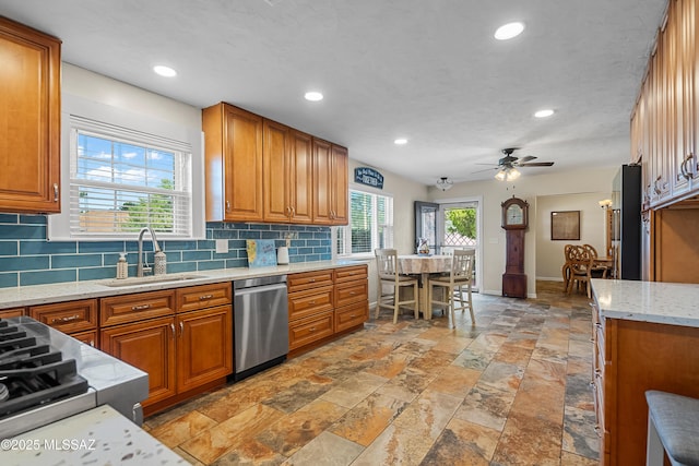kitchen featuring brown cabinetry, stainless steel dishwasher, stone tile flooring, and a sink