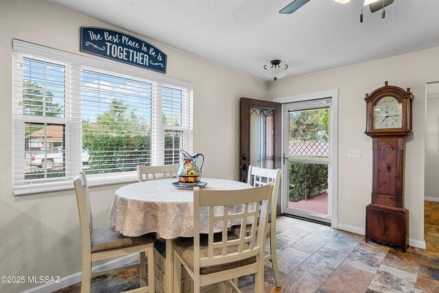dining room featuring stone tile floors, a wealth of natural light, a ceiling fan, and baseboards