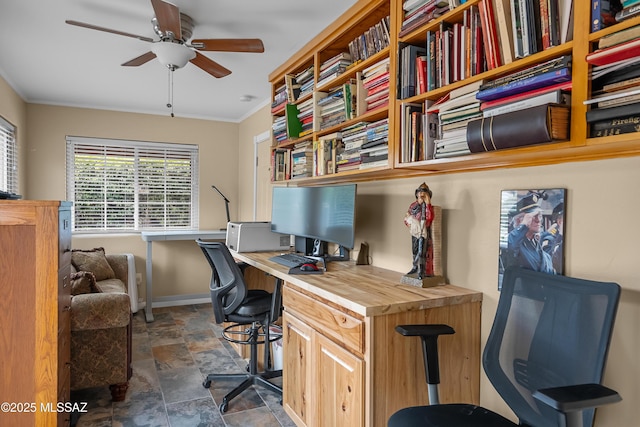office area featuring baseboards, a ceiling fan, stone finish floor, built in study area, and crown molding