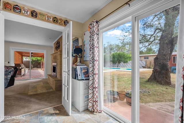 doorway to outside with stone finish flooring, a healthy amount of sunlight, a brick fireplace, and crown molding