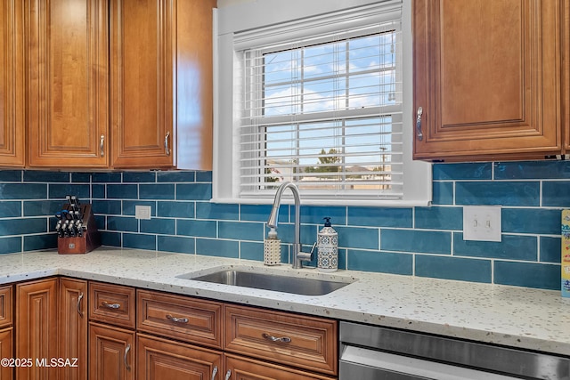 kitchen with decorative backsplash, light stone counters, a sink, and dishwashing machine