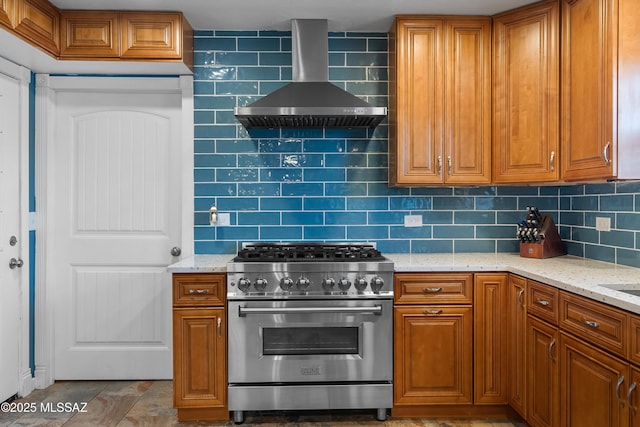 kitchen featuring wall chimney exhaust hood, high end stove, brown cabinets, and tasteful backsplash