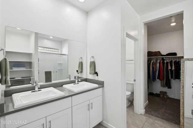 bathroom with double vanity, a walk in closet, tile patterned flooring, and a sink