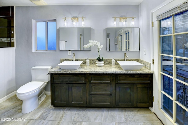bathroom with double vanity, toilet, baseboards, and a sink