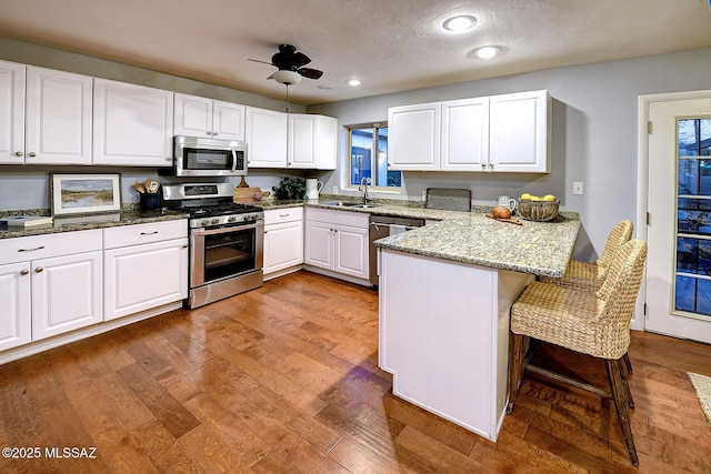 kitchen featuring a kitchen breakfast bar, a sink, stainless steel appliances, a peninsula, and white cabinetry