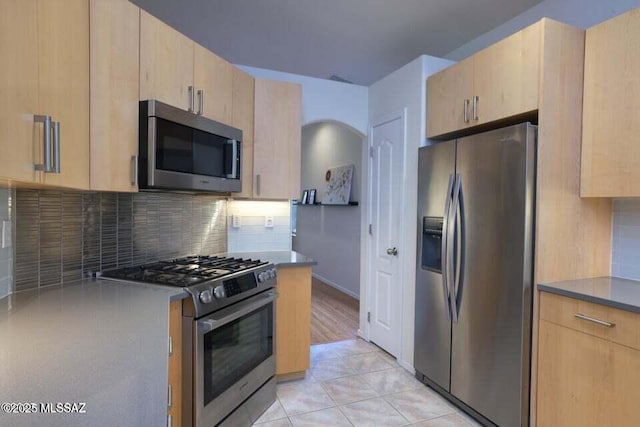 kitchen with light brown cabinets, light tile patterned floors, arched walkways, stainless steel appliances, and backsplash