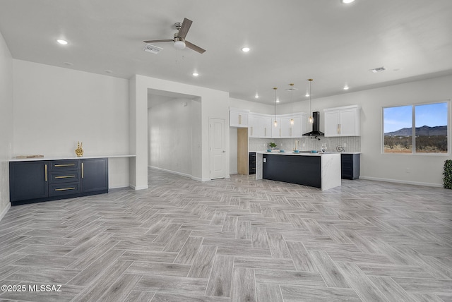 kitchen with wall chimney range hood, a ceiling fan, white cabinets, baseboards, and visible vents