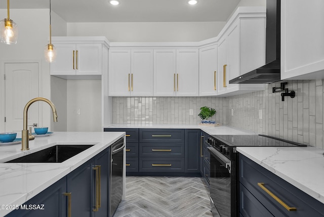 kitchen with wall chimney range hood, appliances with stainless steel finishes, white cabinetry, and a sink