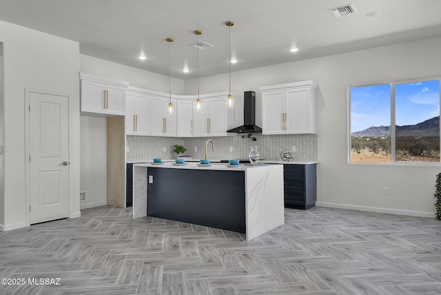 kitchen featuring white cabinets, a kitchen island with sink, visible vents, wall chimney range hood, and light countertops