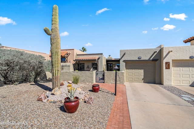 pueblo-style house featuring a gate, stucco siding, concrete driveway, fence private yard, and a garage