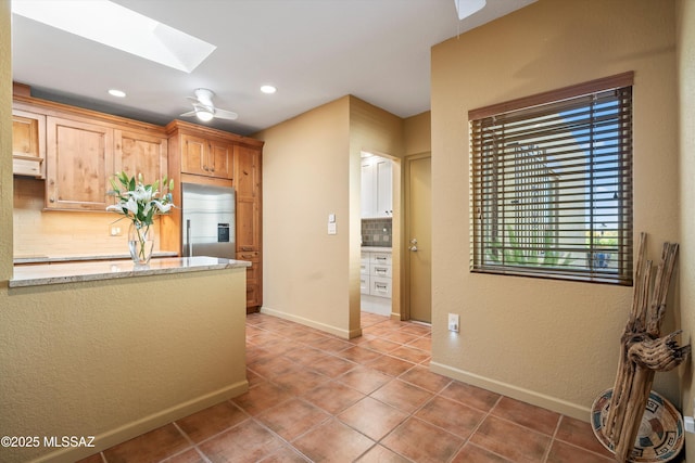 kitchen featuring light tile patterned flooring, tasteful backsplash, stainless steel built in fridge, and a skylight