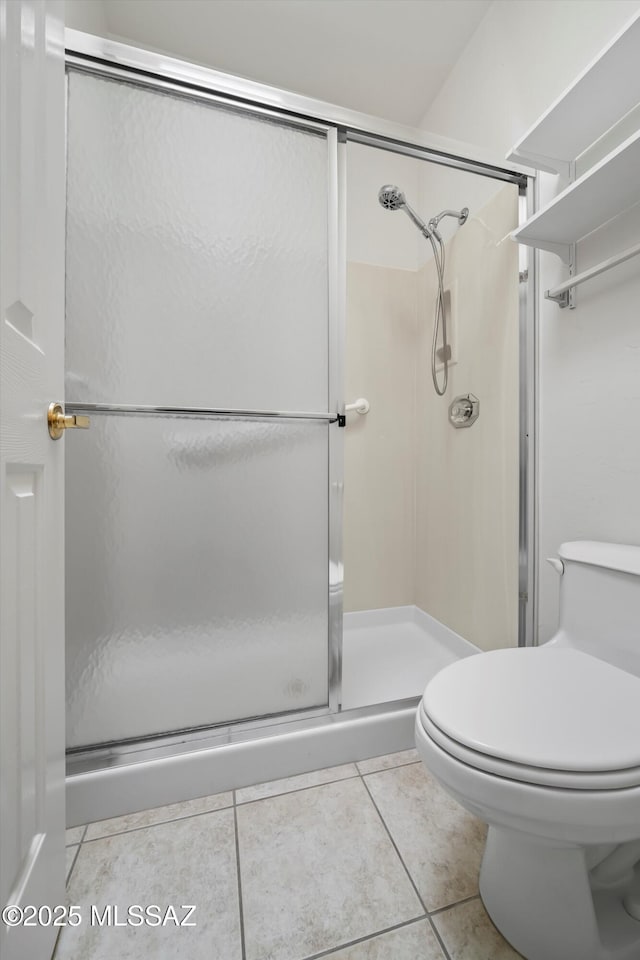 bathroom with a shower stall, toilet, and tile patterned floors