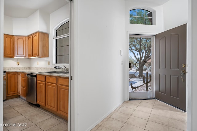 kitchen featuring light tile patterned floors, brown cabinets, a sink, dishwasher, and a high ceiling