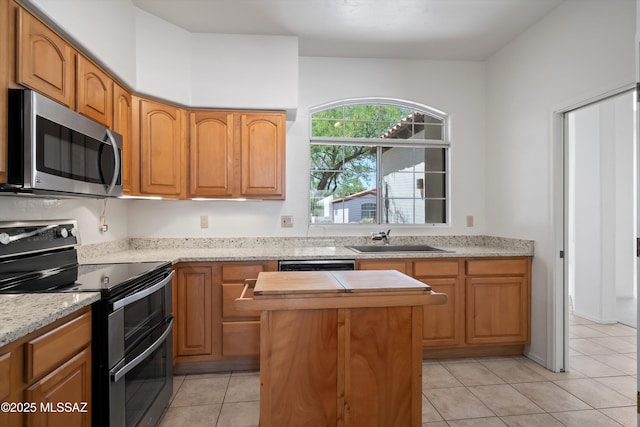 kitchen with light stone counters, light tile patterned floors, a sink, stainless steel appliances, and a kitchen island