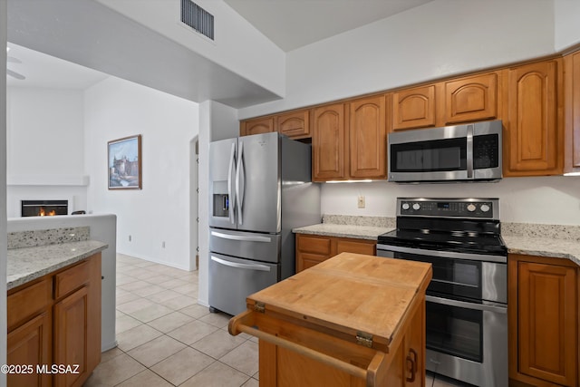 kitchen featuring wood counters, visible vents, stainless steel appliances, light tile patterned flooring, and brown cabinetry