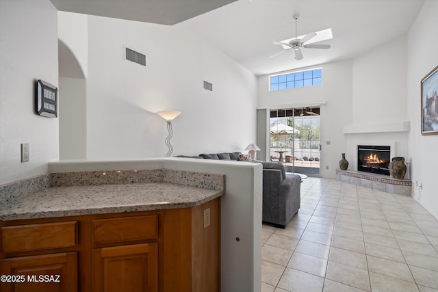 living room with high vaulted ceiling, a ceiling fan, light tile patterned floors, a tiled fireplace, and visible vents