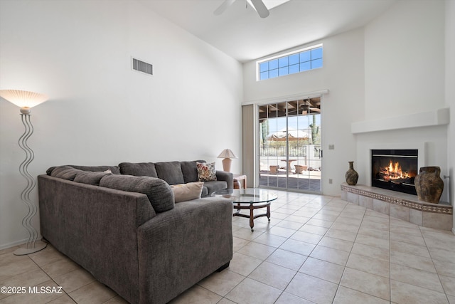living room with light tile patterned floors, a glass covered fireplace, visible vents, a ceiling fan, and high vaulted ceiling