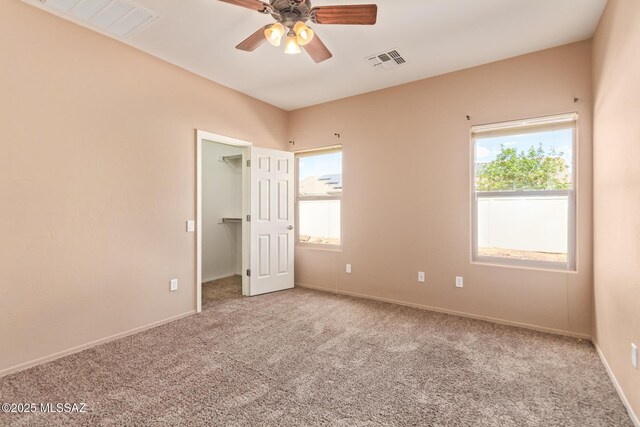 carpeted spare room with visible vents, baseboards, and ceiling fan
