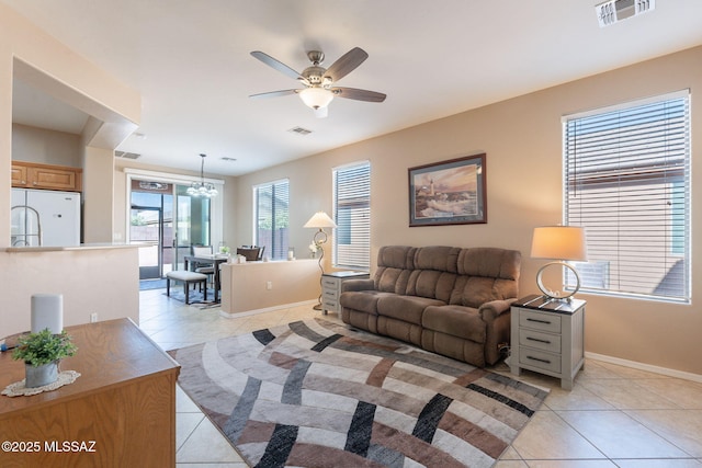 living room featuring ceiling fan with notable chandelier, visible vents, baseboards, and light tile patterned floors