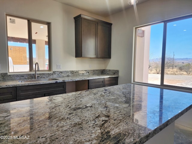 kitchen with light stone countertops, a wealth of natural light, a sink, and dark brown cabinets