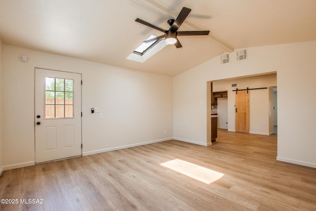 unfurnished room featuring a barn door, light wood-type flooring, baseboards, vaulted ceiling with skylight, and a ceiling fan