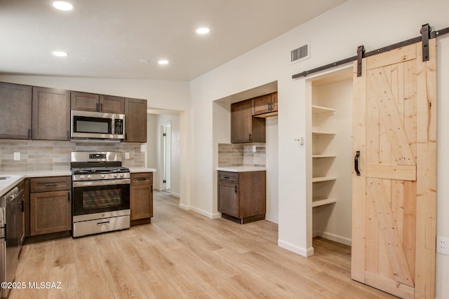 kitchen featuring a barn door, visible vents, backsplash, light countertops, and appliances with stainless steel finishes
