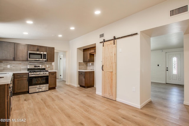 kitchen featuring a barn door, backsplash, stainless steel appliances, and visible vents