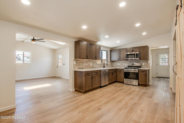 kitchen featuring light wood finished floors, tasteful backsplash, lofted ceiling, light countertops, and appliances with stainless steel finishes