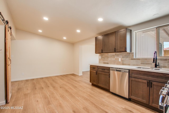 kitchen with stainless steel dishwasher, a sink, tasteful backsplash, light wood-style floors, and light countertops