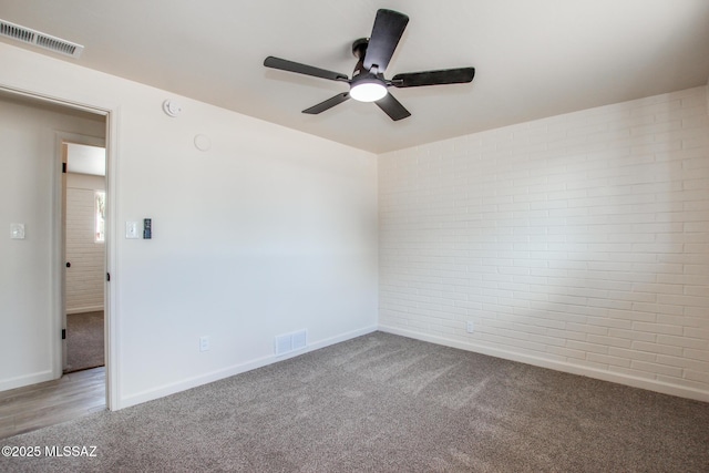 carpeted spare room with visible vents, brick wall, baseboards, and ceiling fan