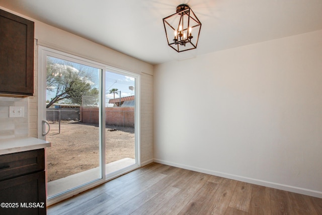 unfurnished dining area with baseboards, a notable chandelier, and light wood finished floors