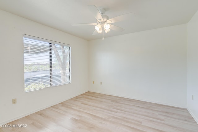 spare room with light wood-type flooring, a ceiling fan, and baseboards