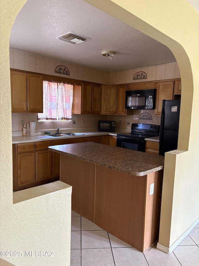 kitchen with a sink, visible vents, black appliances, brown cabinetry, and light tile patterned floors