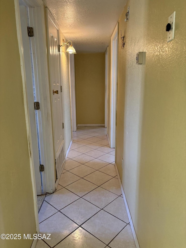 corridor featuring baseboards, a textured ceiling, and light tile patterned flooring
