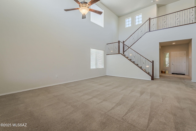 unfurnished living room featuring ceiling fan, light carpet, stairs, and a towering ceiling
