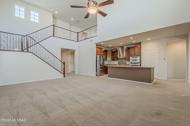 unfurnished living room with ceiling fan, visible vents, light carpet, and a towering ceiling
