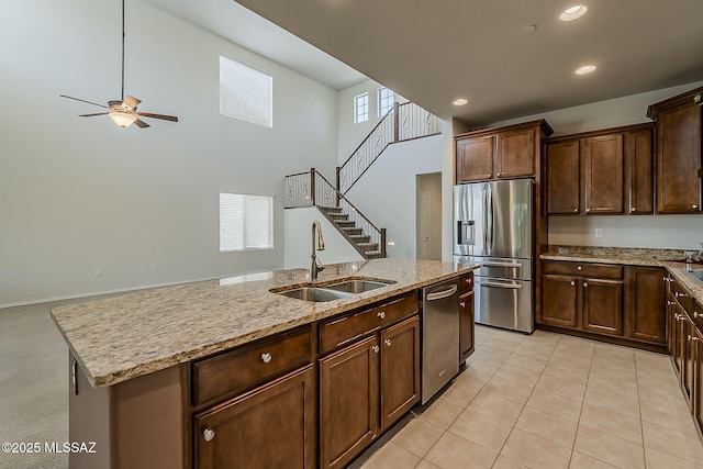 kitchen featuring light stone countertops, a sink, stainless steel appliances, a ceiling fan, and a towering ceiling