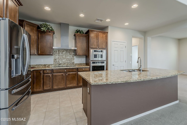 kitchen featuring wall chimney range hood, visible vents, a sink, light stone counters, and stainless steel appliances