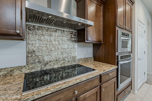 kitchen with stainless steel oven, black electric stovetop, wall chimney range hood, light stone counters, and light tile patterned floors