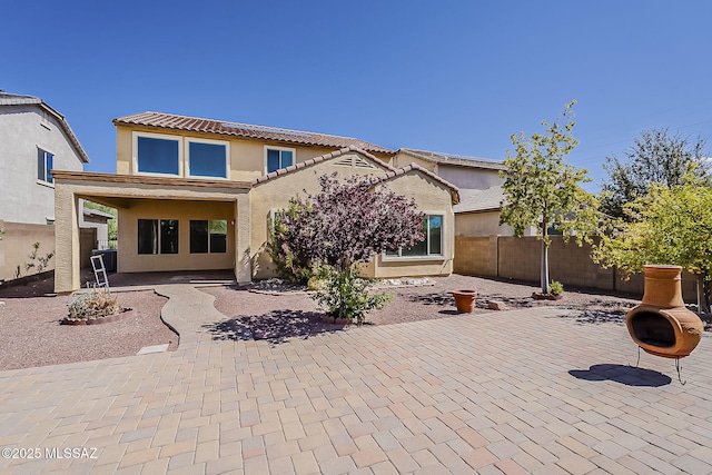 rear view of property with fence, stucco siding, a patio area, and a tile roof