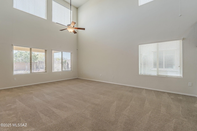 empty room featuring a ceiling fan, baseboards, light colored carpet, and a towering ceiling