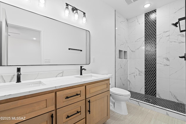 bathroom featuring a tile shower, double vanity, toilet, and a sink
