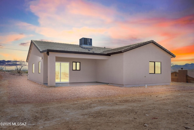 back of house at dusk featuring central air condition unit, a patio, a tiled roof, and stucco siding