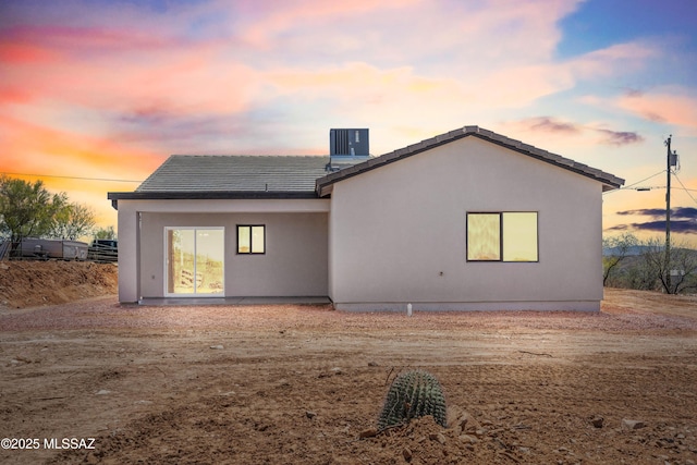 back of house featuring a tile roof, central AC, and stucco siding