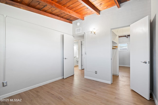 unfurnished bedroom with visible vents, beam ceiling, a walk in closet, wooden ceiling, and light wood finished floors