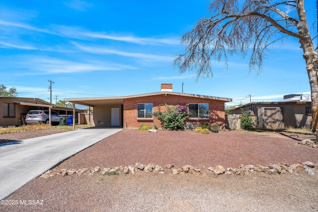 view of front facade featuring concrete driveway, brick siding, a chimney, and a carport