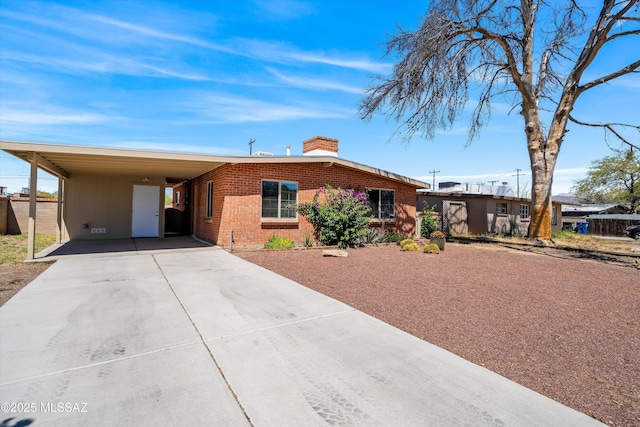 view of front of home with a carport, a chimney, concrete driveway, and brick siding
