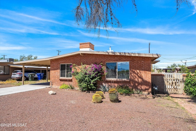 view of front of property featuring concrete driveway, brick siding, a chimney, and an attached carport