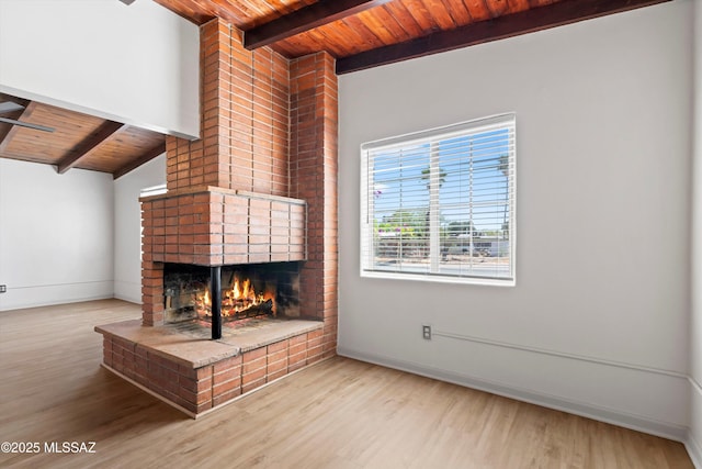 unfurnished living room featuring beam ceiling, a fireplace, baseboards, wood finished floors, and wood ceiling