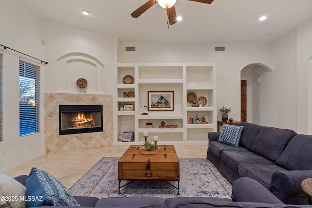 living area featuring light tile patterned floors, arched walkways, ceiling fan, and built in shelves